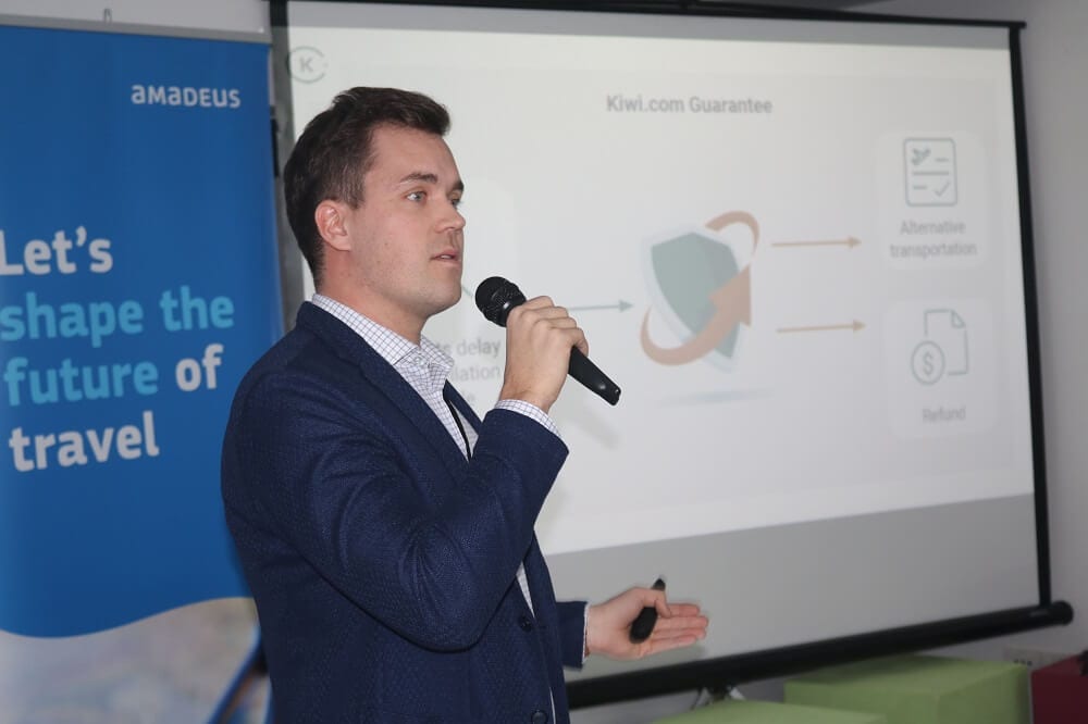 Predavač u tamnoplavom sakou govori uz slajd o jamstvu Kiwi.com