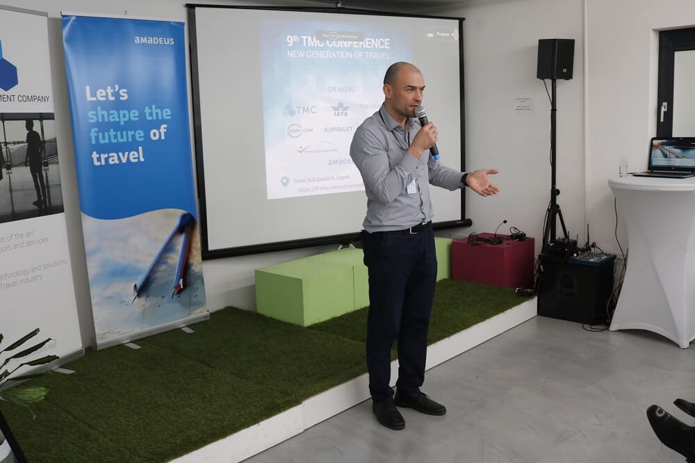 Govornik s mikrofonom ispred platna s naslovnicom 9. TMC konferencije
